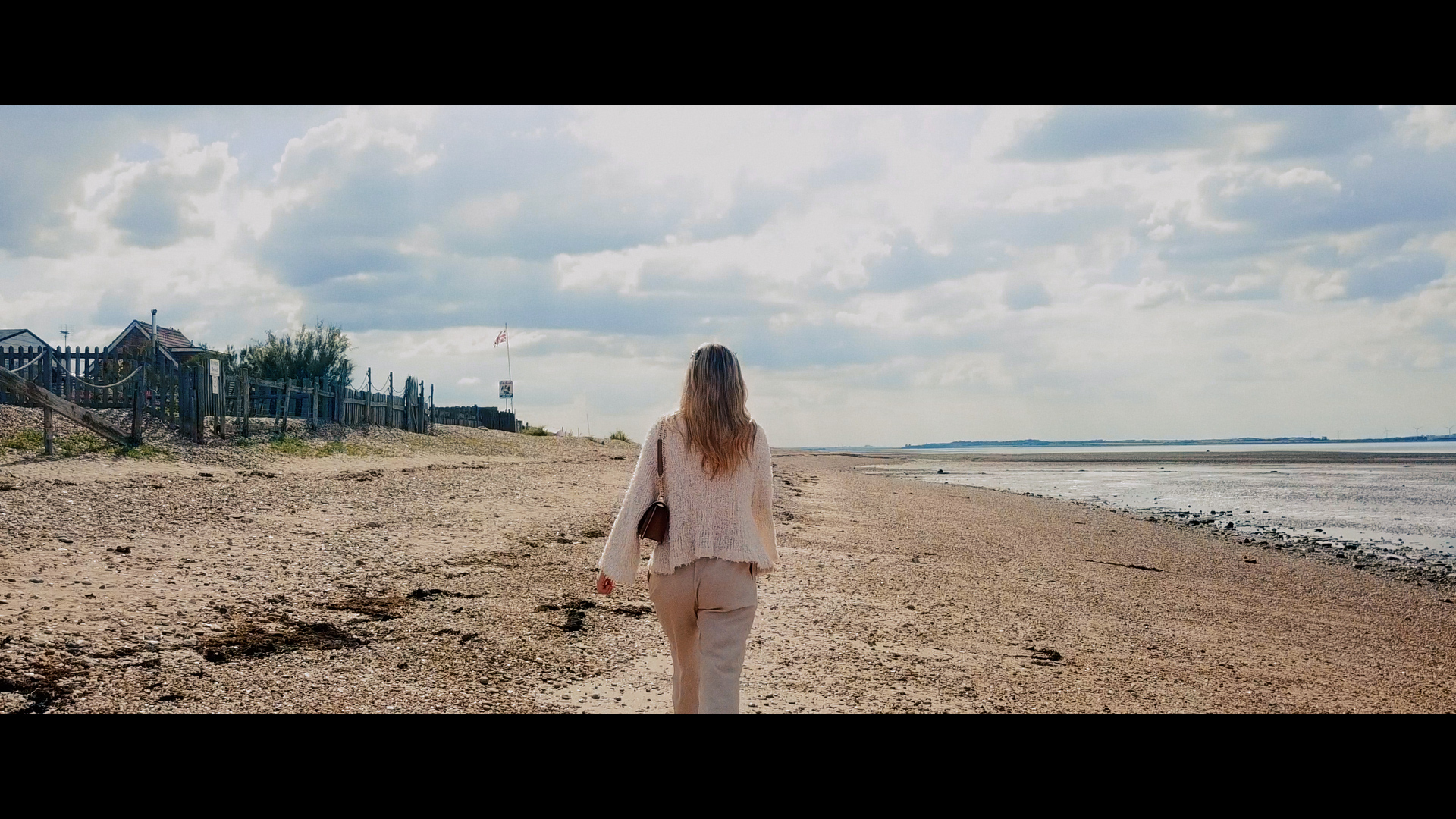 Jazzy Whipps walking away from the camera on the beach with the sea on her right.